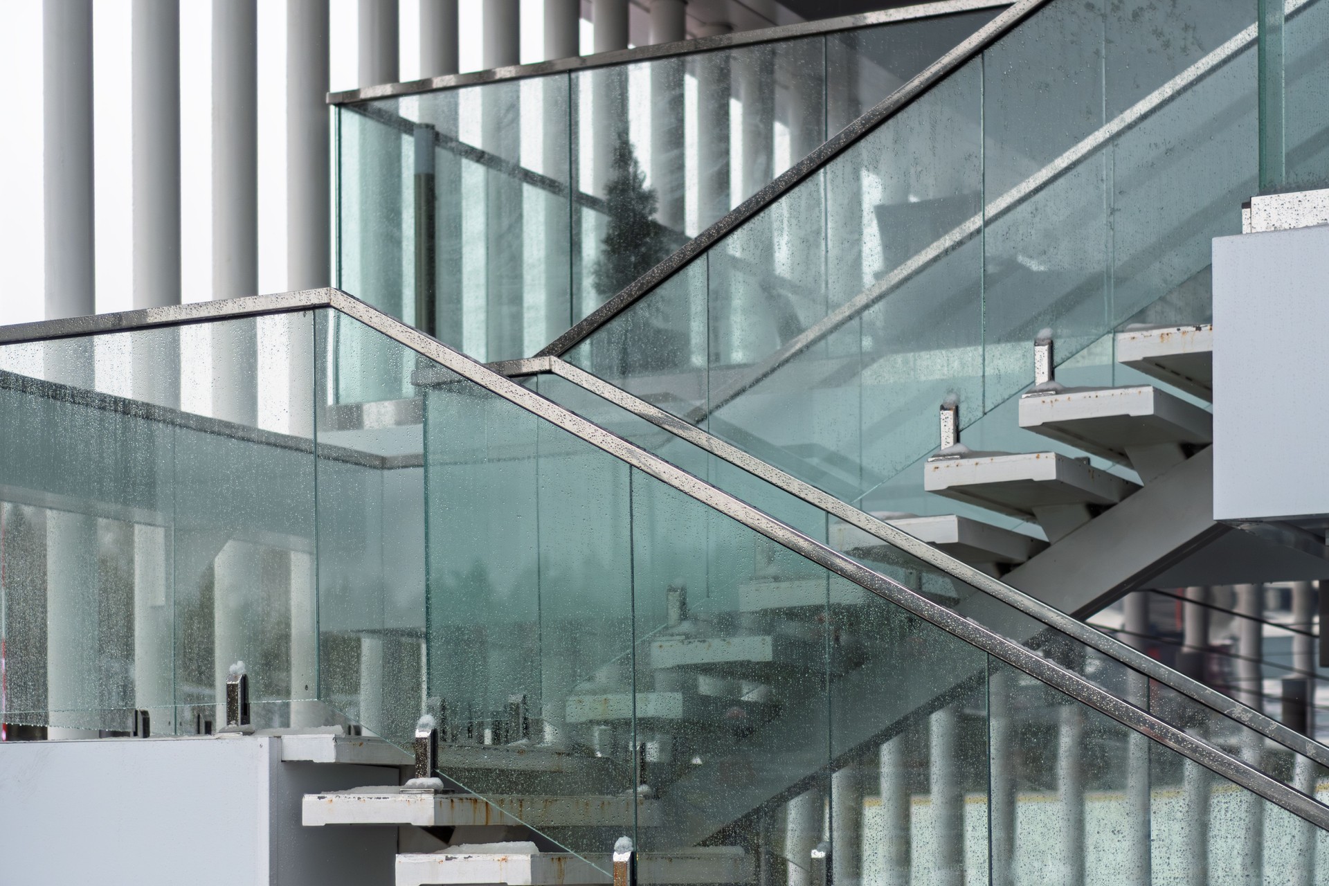 Modern staircase with glass railings and steel details reflects minimalism and geometry, while raindrops add texture and depth to the scene.